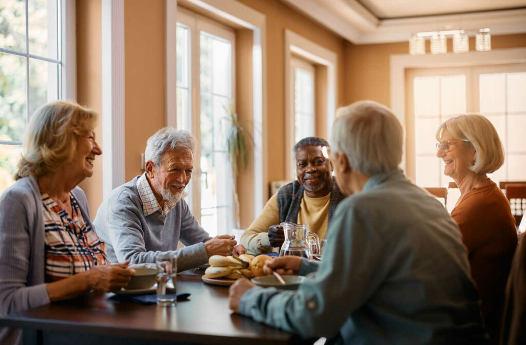 A group of seniors sitting around a table smiling, eating and chatting with each other.