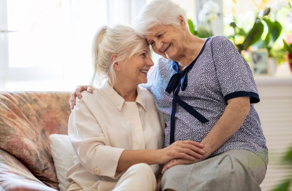 An adult and their older parent hug on the couch, enjoying a moment of joy as they navigate their changing relationship